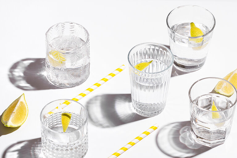 Wassergläser mit Zitronenscheiben und gelb-weißen Strohhalmen.
