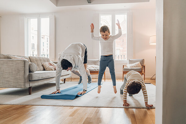 Vater macht mit seinen 2 Söhnen ein Home-Workout im Wohnzimmer.