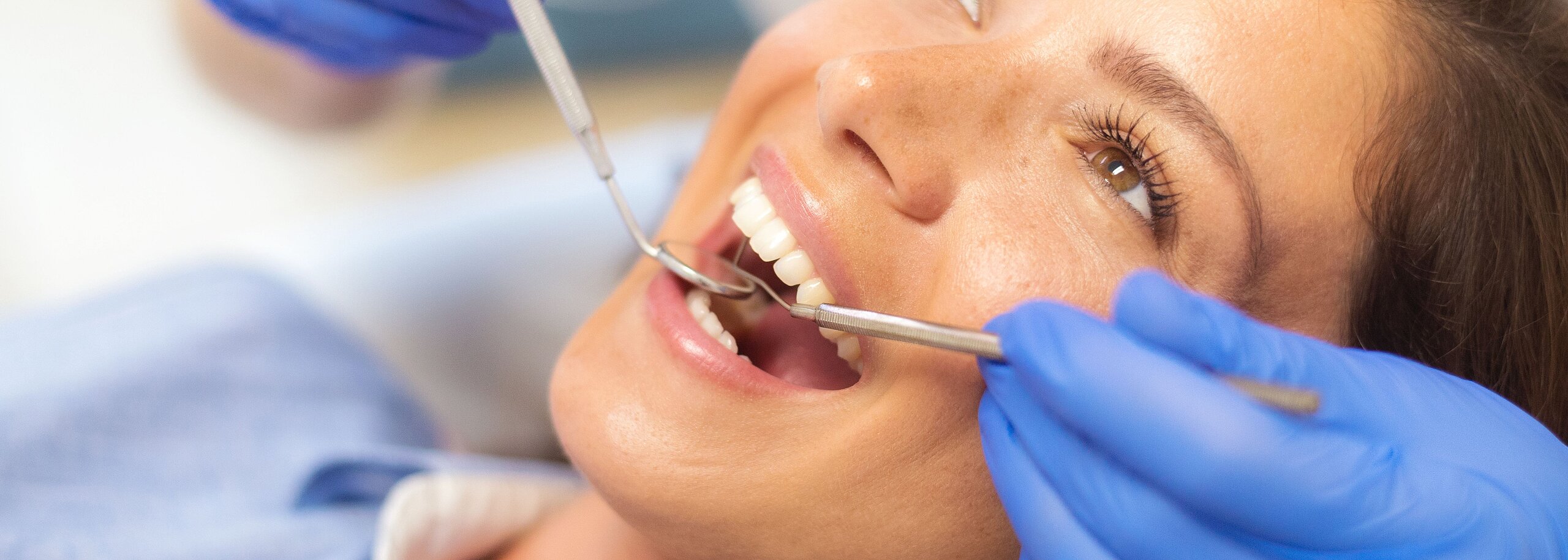 Eine Frau liegt auf dem Zahnarztstuhl und hat den Mund geöffnet zur Kontrolle