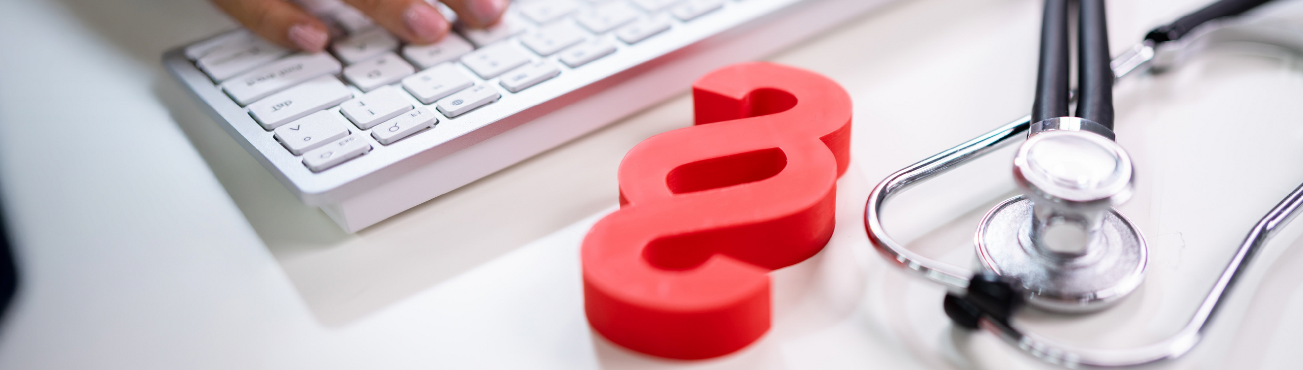 Ein rotes Paragraphenzeichen liegt neben einem Stethoskop auf dem Tisch.