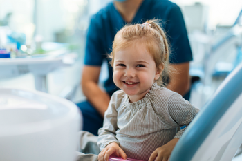 Kleines Mädchen sitzt lachend auf dem Behandlungsstuhl beim Zahnarzt
