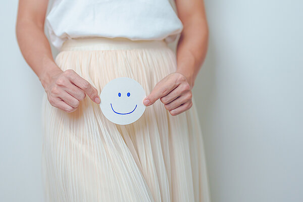 Frau hält glücklichen Smiley vor ihren Unterleib.