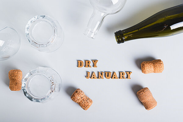 Korken, leere Gläser und Flaschen liegen auf einem Tisch. In der Mitte der Schriftzug "Dry January".