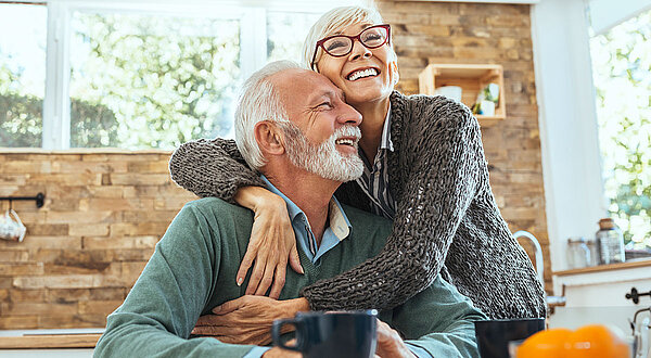 Ältere Frau umarmt älteren Mann, beide lachen