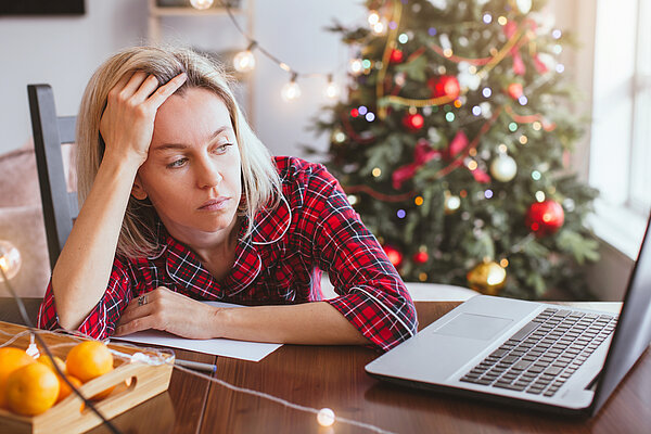 Frau sitzt gestresst am Tisch vor ihrem Laptop in der Weihnachtszeit.