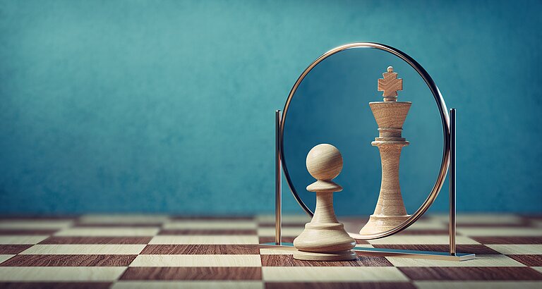 Bauer Schachfigur steht vor einem Spiegel. Im Spiegel ist die Schachfigur König zu sehen.