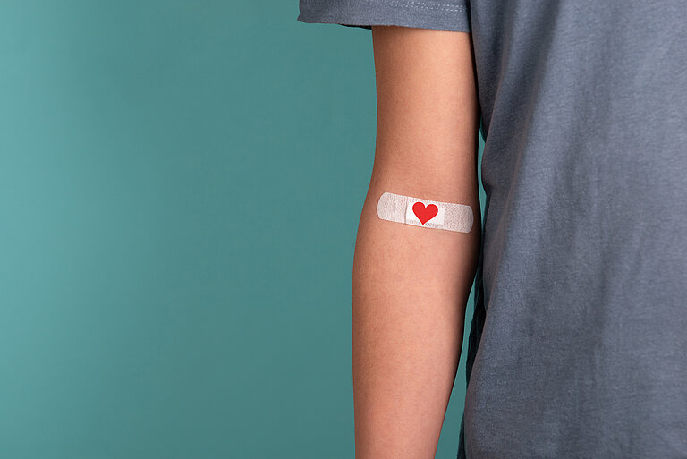 Arm nach einer Blutspende mit Pflaster, auf dem ein Herz ist. 