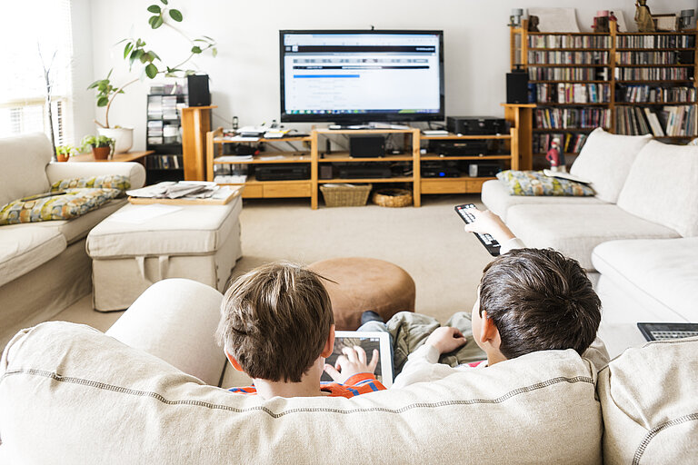 2 Jungen sitzen auf dem Sofa und schauen TV.