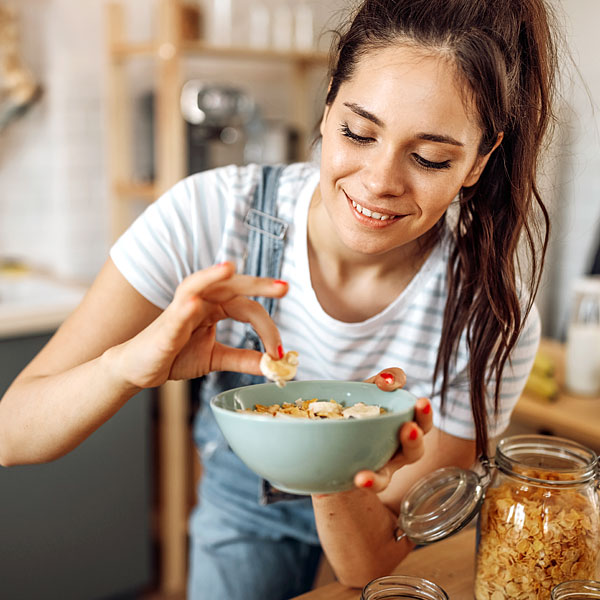 Eine junge Frau in einer Küche mit einer Schüssel mit Müsli in der Hand und lächelt dabei.