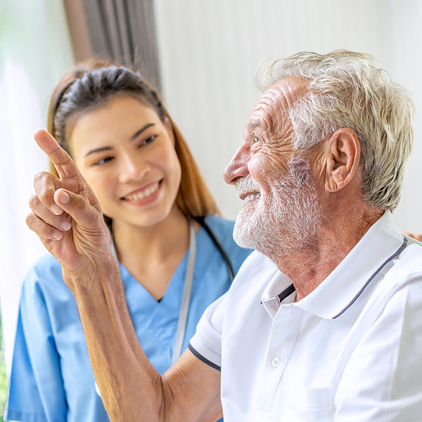 weibliche Pflegekraft und älterer Mann sitzen zusammen und lächeln.