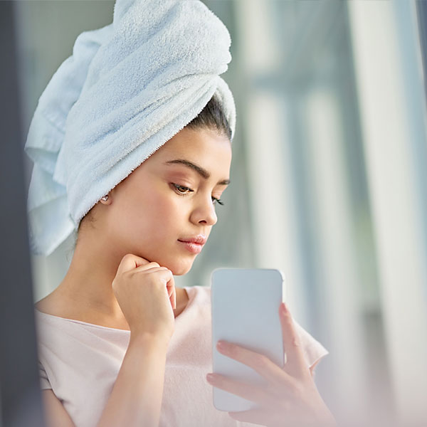Junge Frau mit Handtuch auf dem Kopf macht ein Bild von sich im Spiegel. 