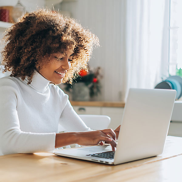 Junge Frau sitzt am Laptop und lächelt.