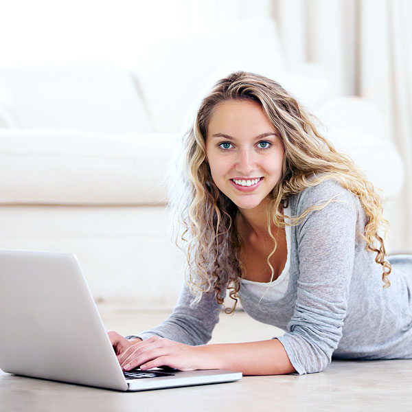 Junge Frau liegt auf dem Bauch, vor ihr ein Laptop.