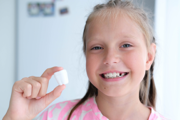 Mädchen hält eine kleine Milchzahndose zwischen den Fingern und lächelt.