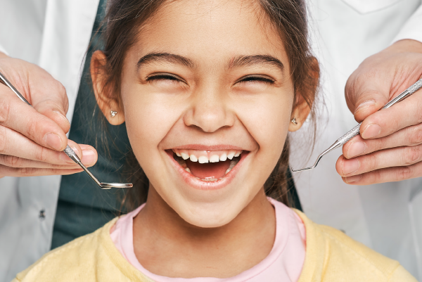 Ein kleines Mädchen ist zur Kontrolle beim Zahnarzt und  lacht über beide Ohren